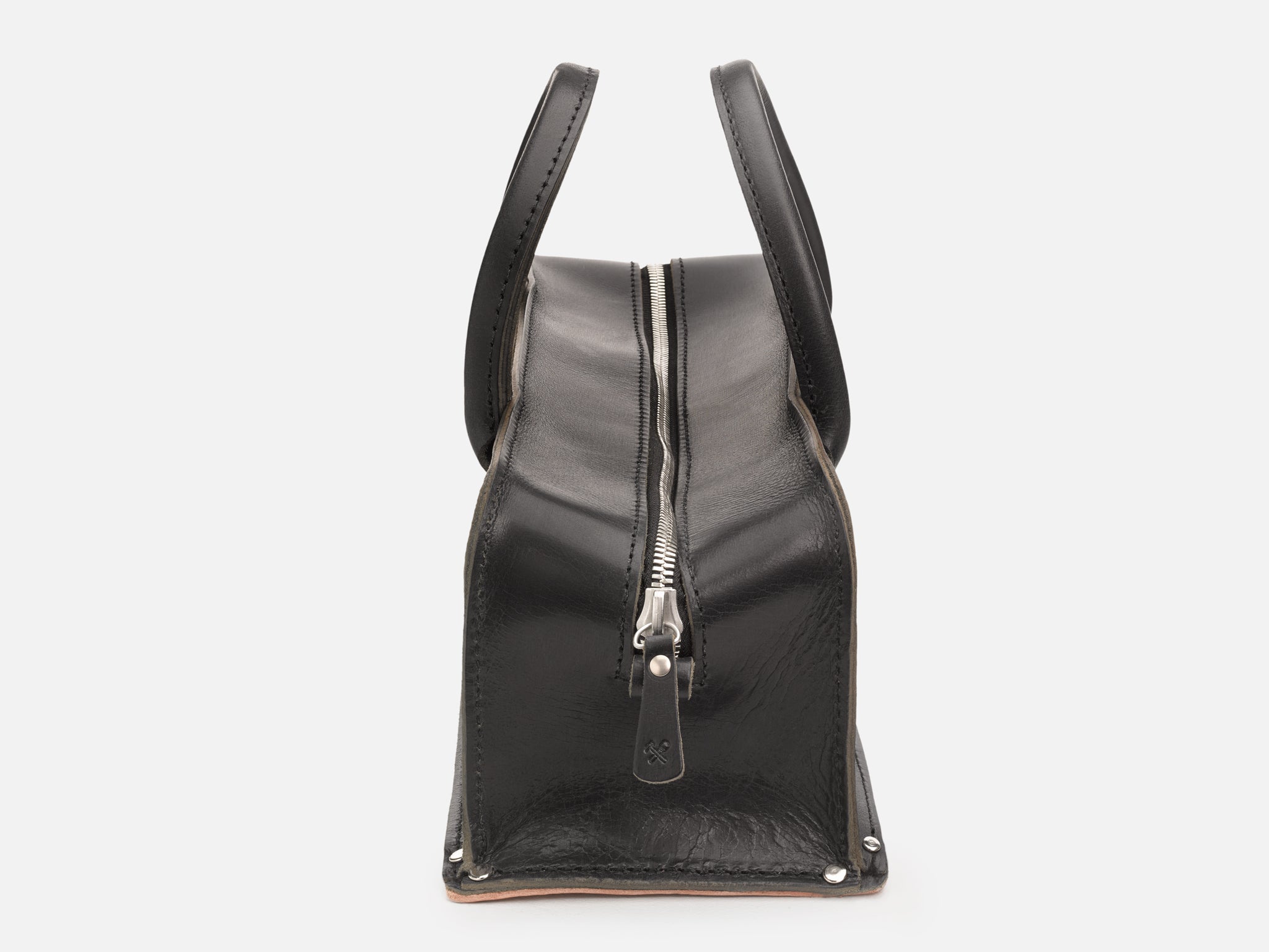 A side view of a black leather tool bag with rivet reinforced corners and silver zipper set in a white background