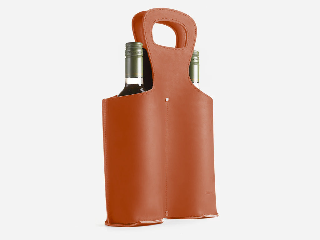 A brown leather wine tote holds two bottles of wine, with handles at the top for easy carrying. The sleek, minimalist design stands upright against a plain white background.