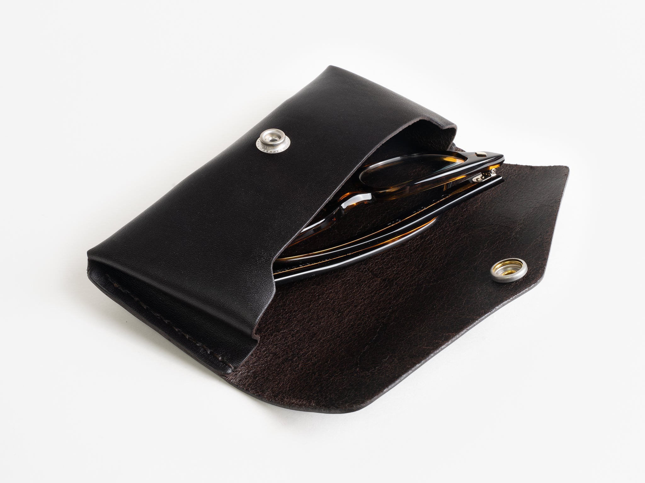 A pair of sunglasses partially visible inside an open black leather case with a snap button closure, set against a white background.
