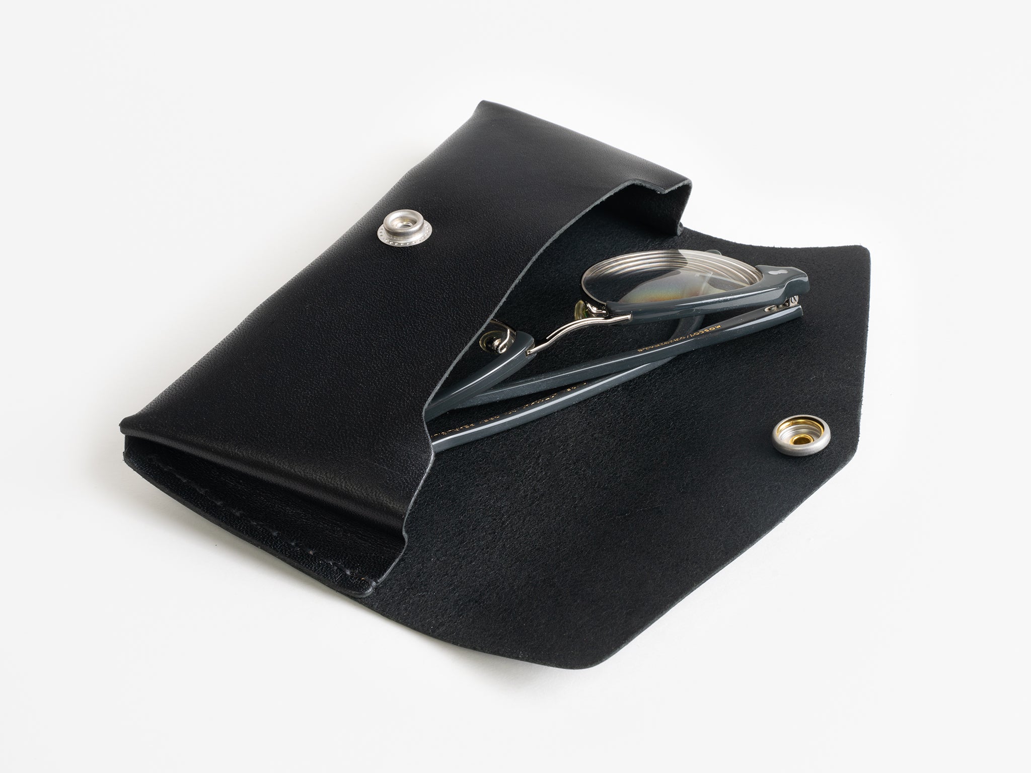 A black leather pouch partially open, revealing a pair of metal nail clippers inside. The pouch has a silver snap button and is set on a plain white surface.