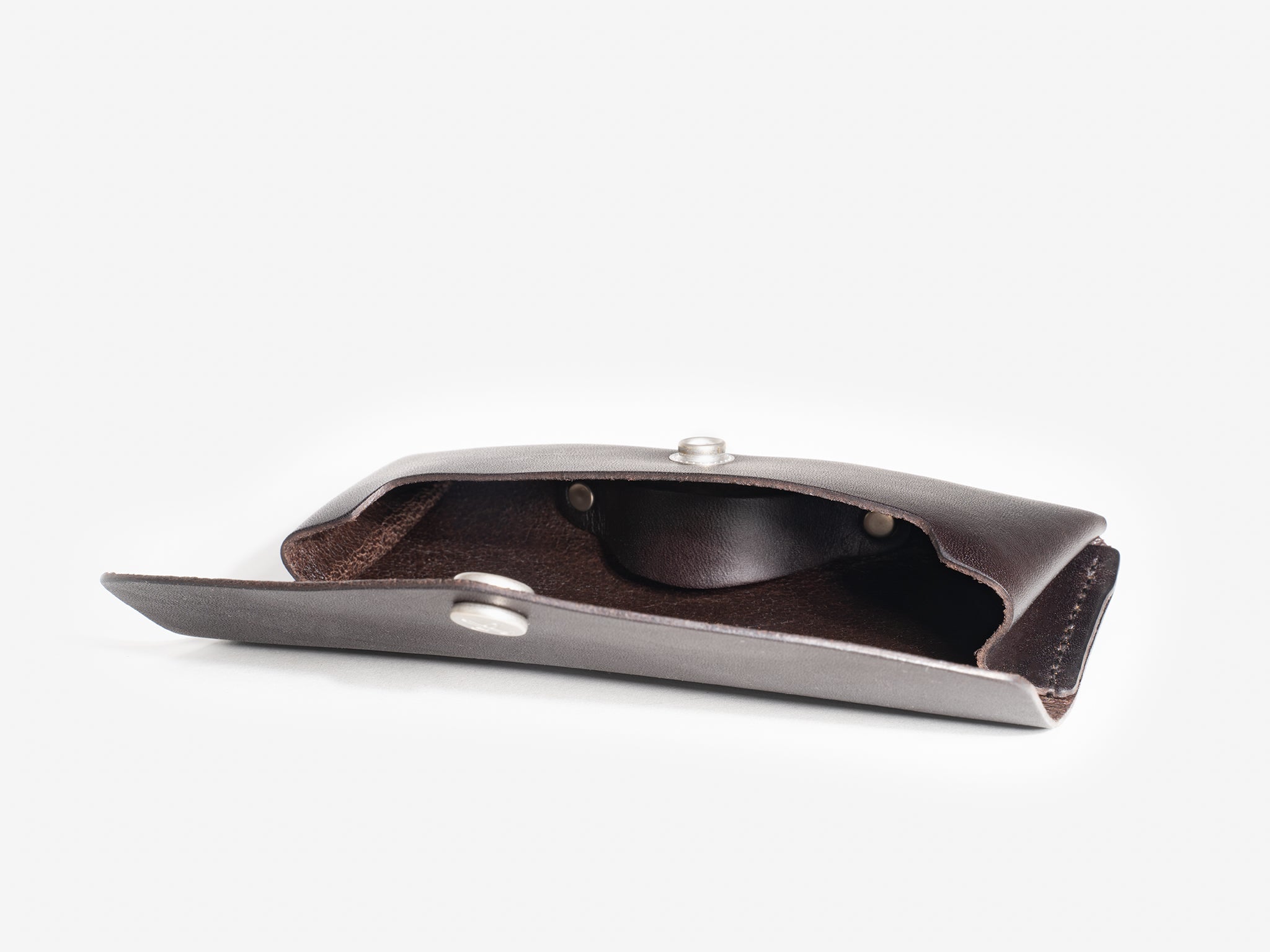 A brown leather eyeglass case with metal snap buttons is shown open on a white background, revealing its soft inner lining.