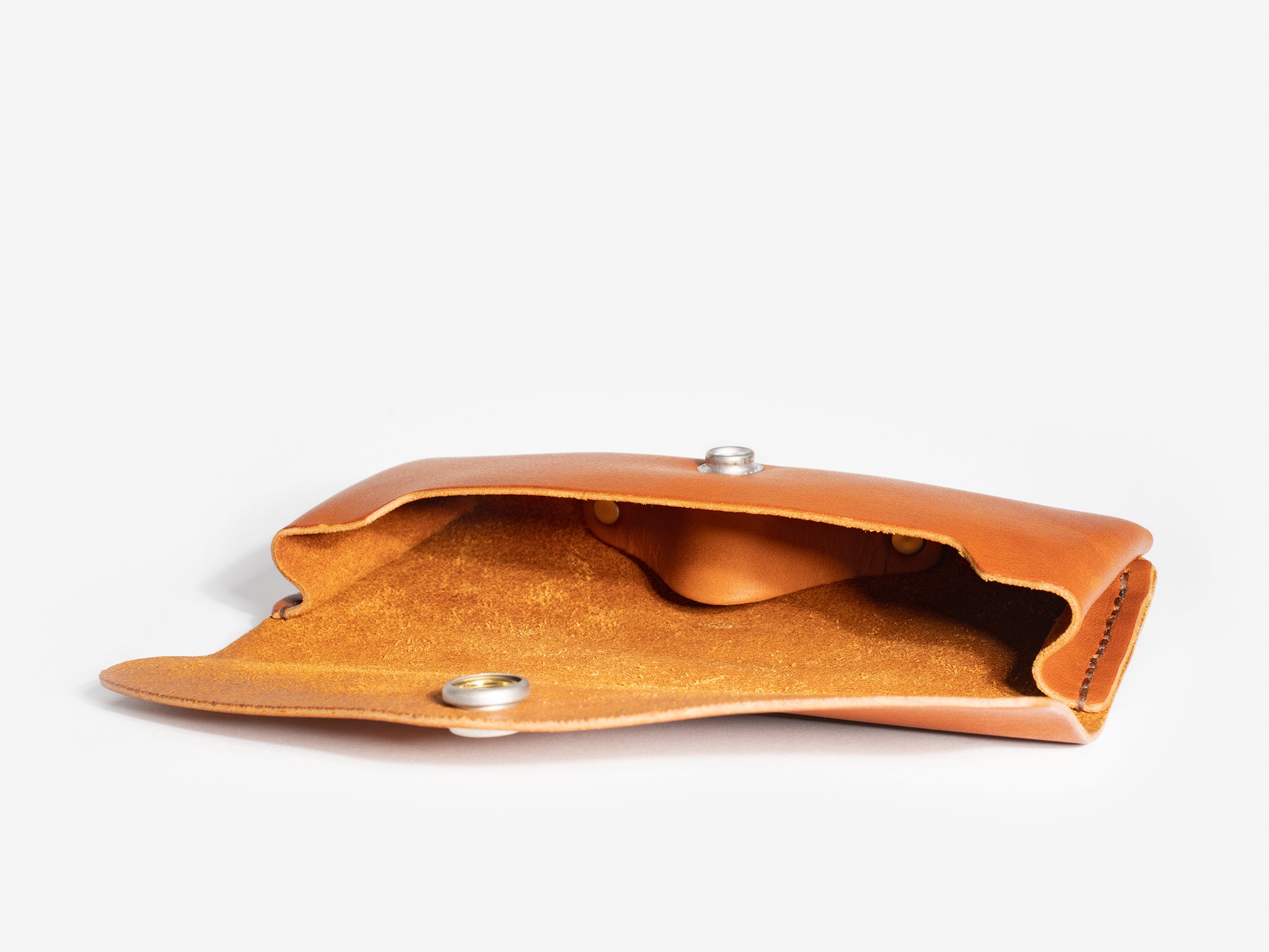 A small, tan leather pouch with a snap button closure is open, revealing its suede interior. The pouch is placed on a plain white background.