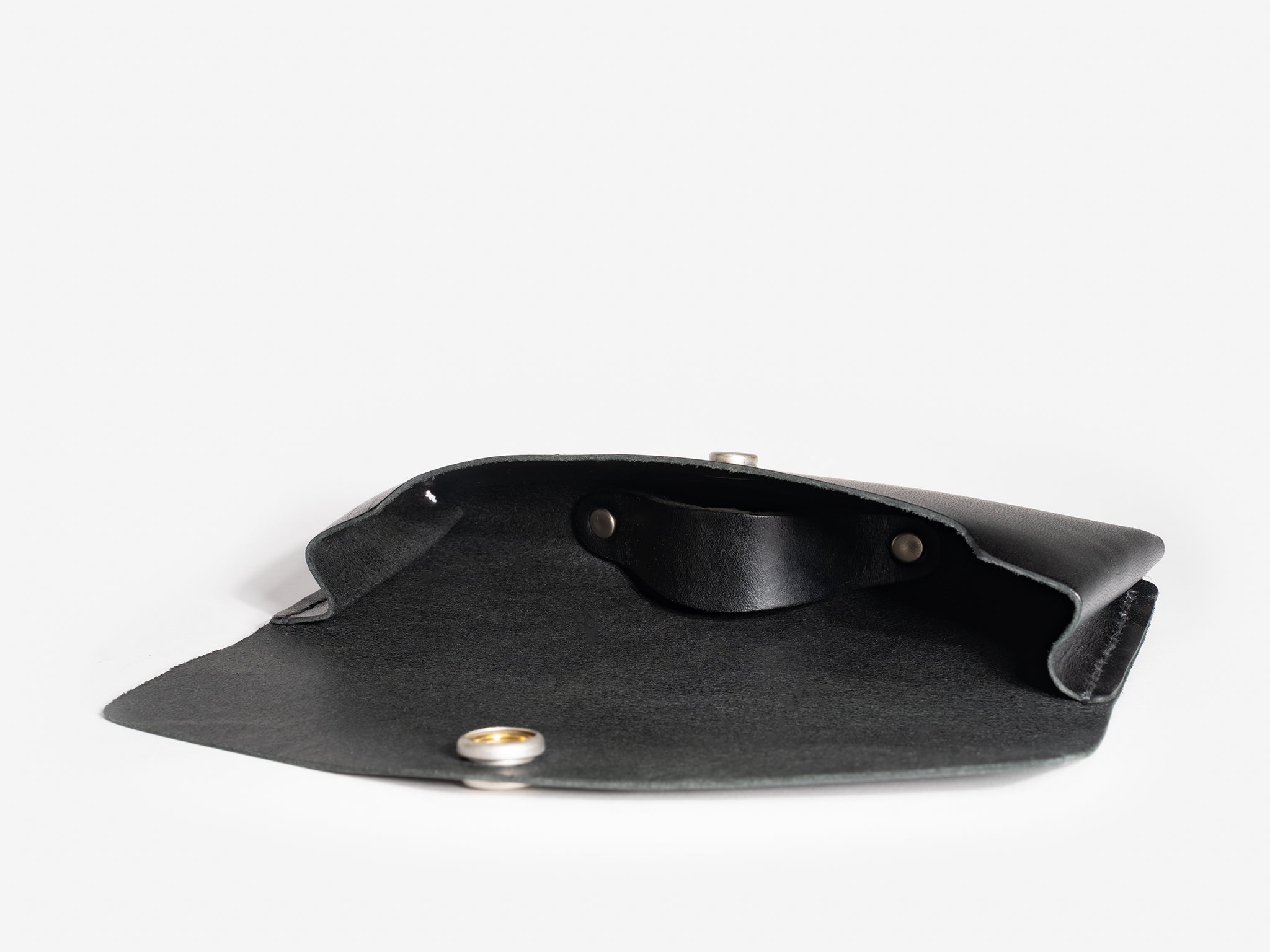 An open black leather pouch with a snap button closure lying on a white surface, showing the inside lining and metal fasteners.