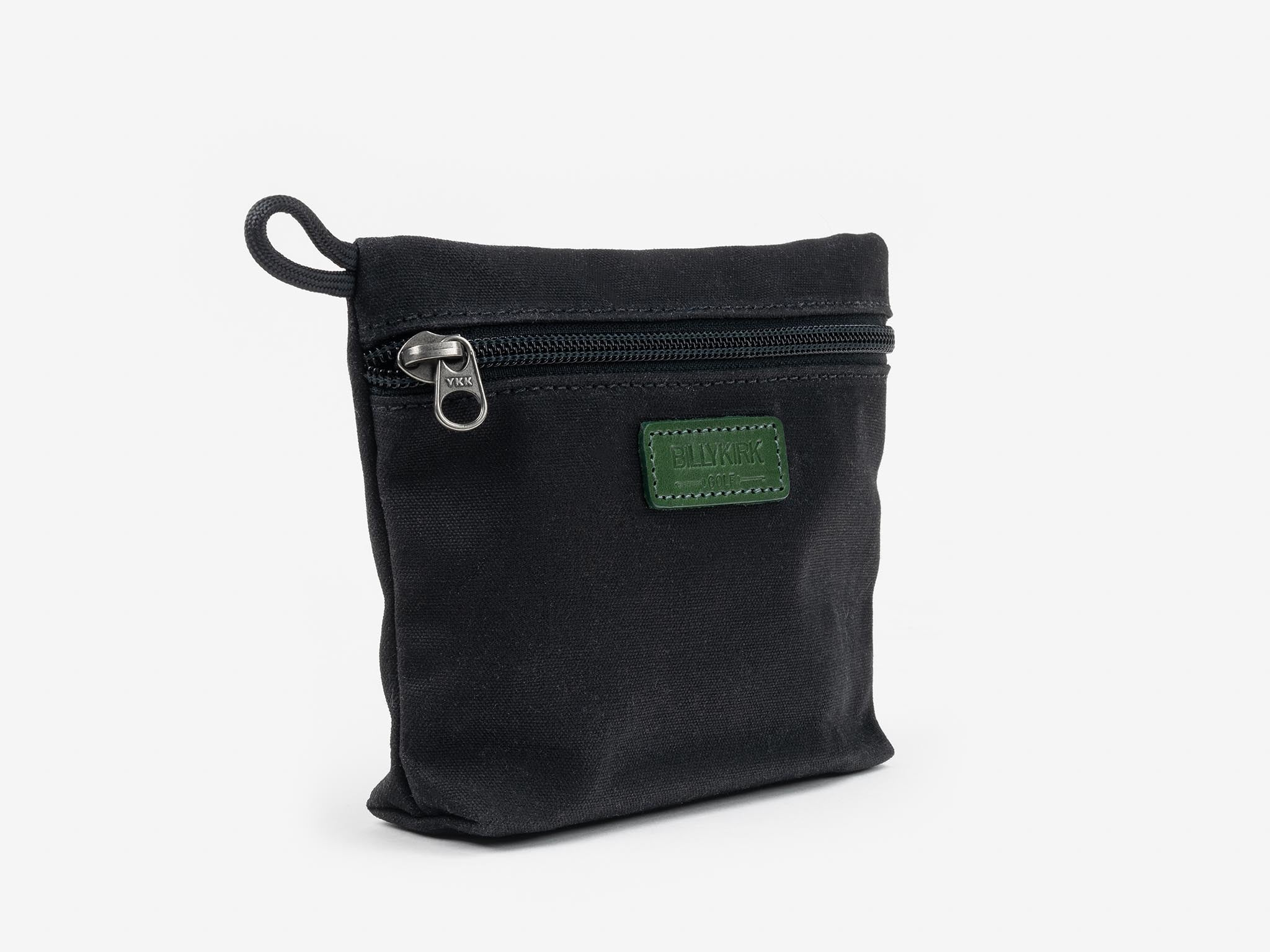 A small black fabric pouch with a zippered closure and a loop on one side. It features a green rectangular patch with stitching detail and embossed text on the front. The background is plain white.