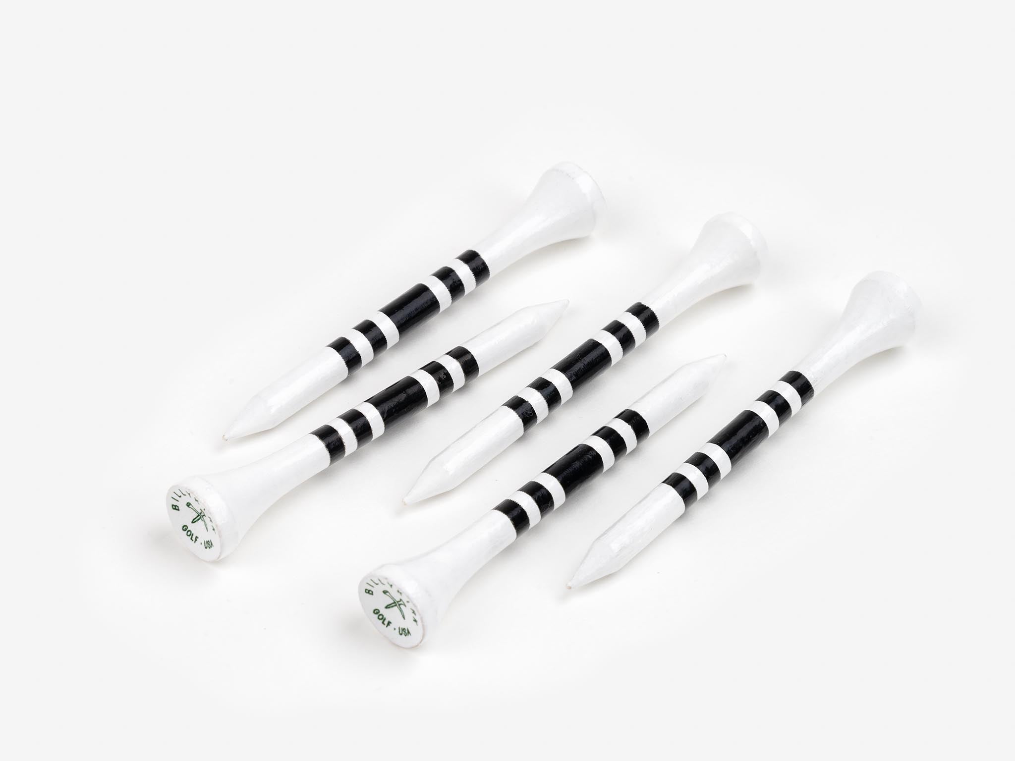 Five white golf tees with three black stripes each are arranged in a scattered pattern on a plain white background. The tops of the tees have a small white circle with a green logo and numbers.