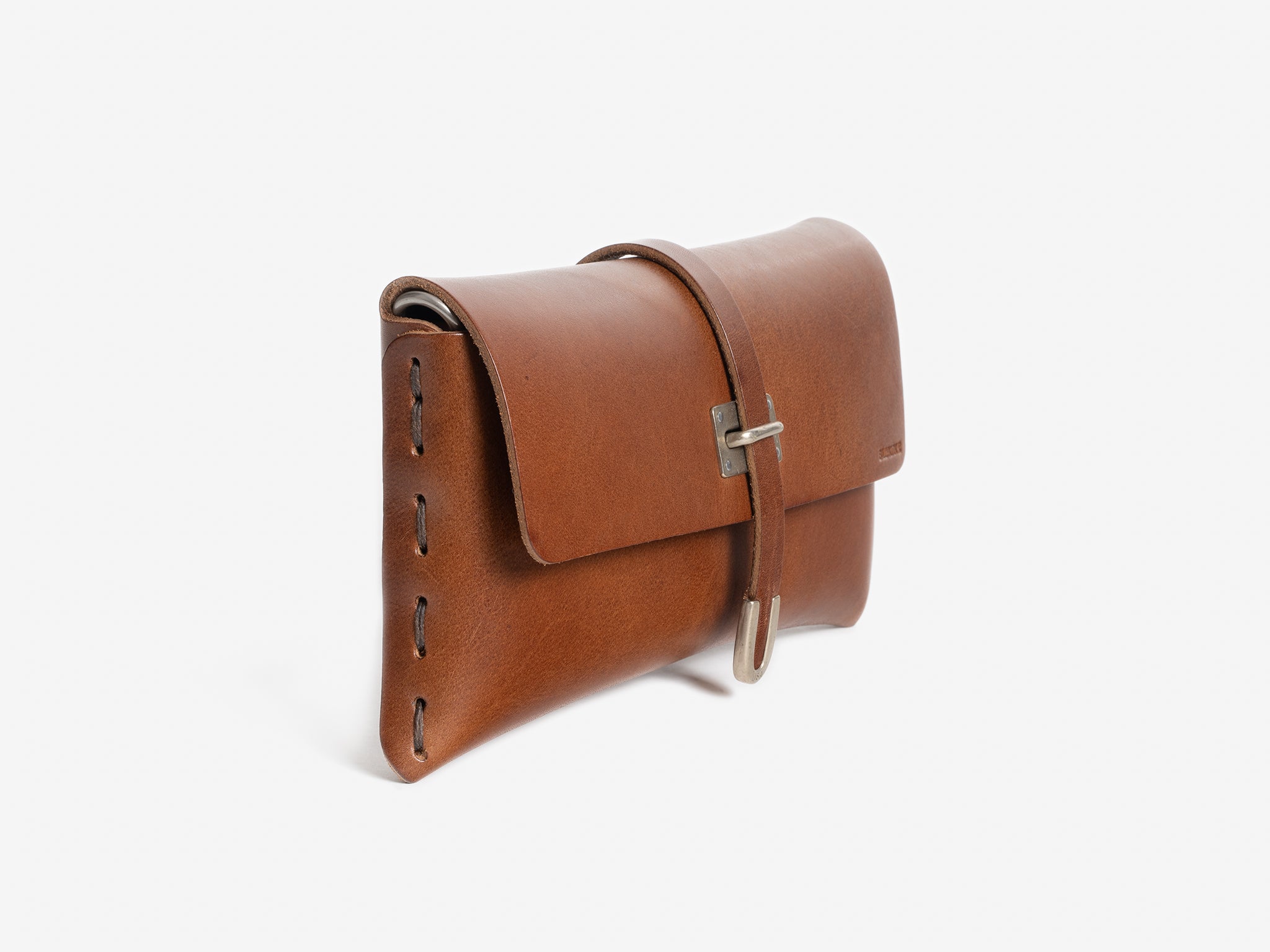 A brown leather clutch purse with a stitched side seam, flap closure, and a strap with a silver buckle, photographed on a white background.