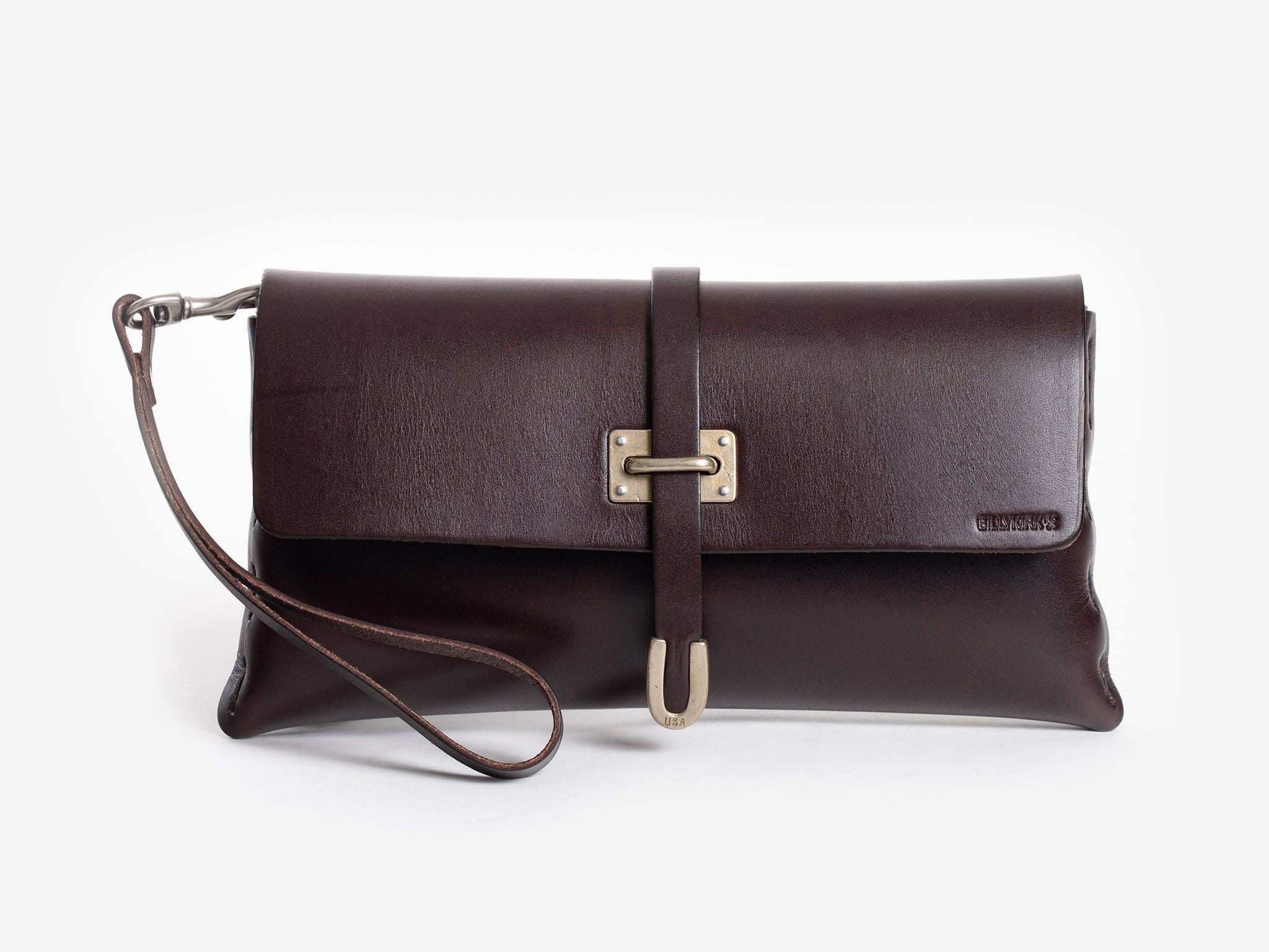 A dark brown leather clutch bag with a wrist strap, front flap closure, and a decorative brass buckle. The brand name is embossed on the lower right corner of the flap.