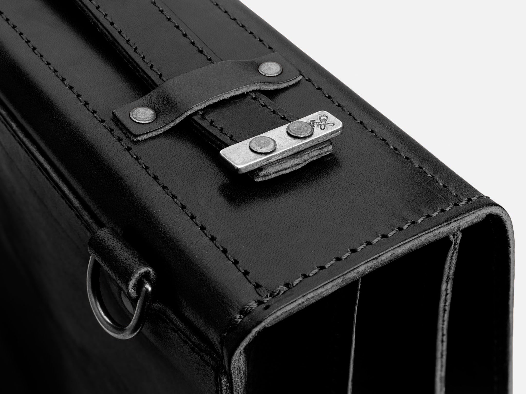 Close-up of a black leather bag featuring detailed stitching, a metal clasp with two rivets, and a D-ring on the side, set against a plain white background.
