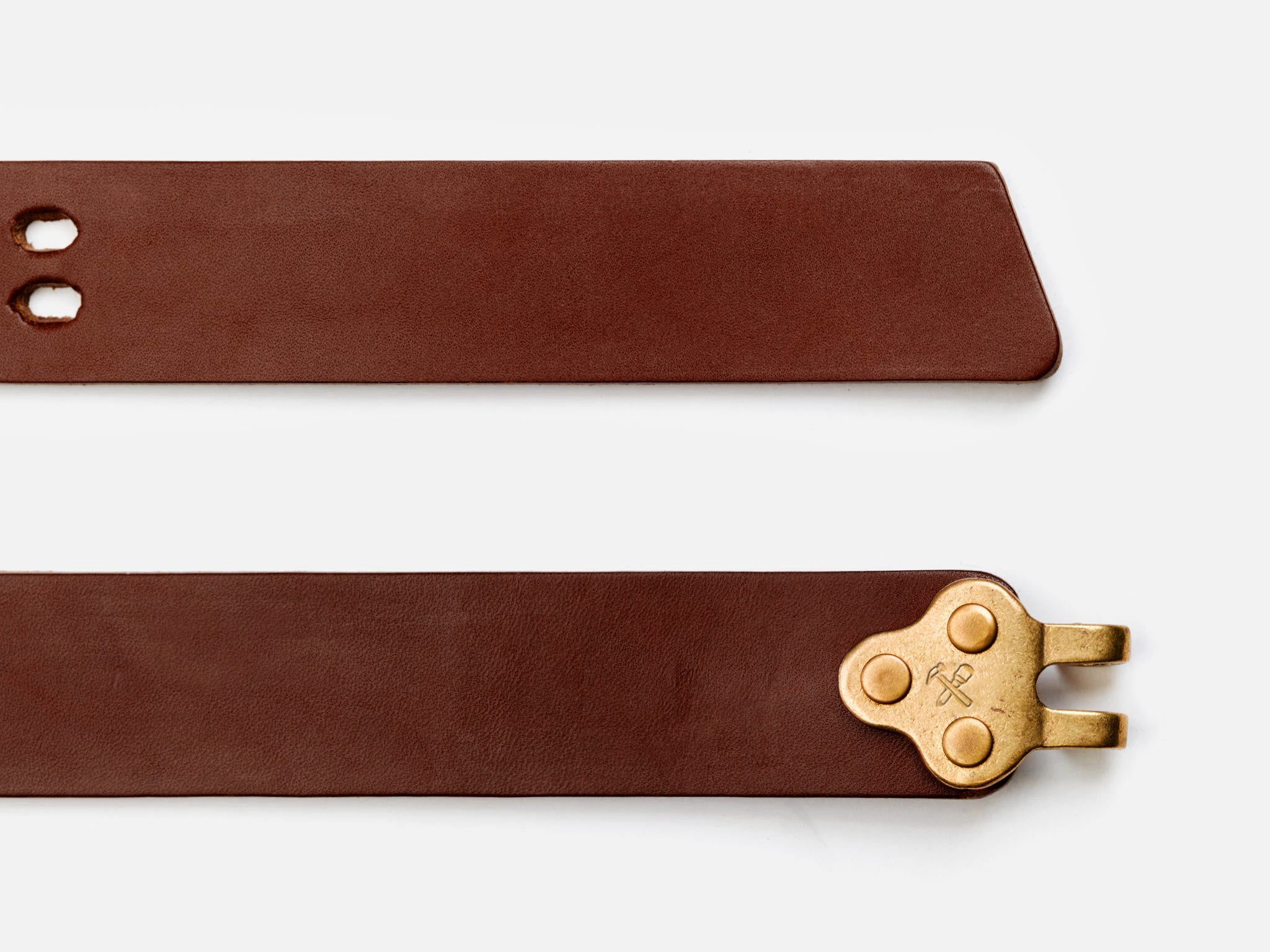 A brown leather belt with a brass buckle featuring an engraved symbol. The belt is shown from two angles: one with a pointed end and two holes, and one with the buckle end visible.
