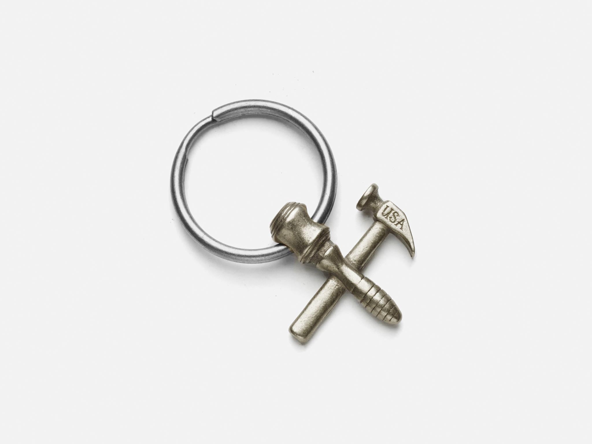 A metal keyring featuring a miniature hammer and screw crossed together, with the word USA engraved on the hammers head, set against a plain white background.
