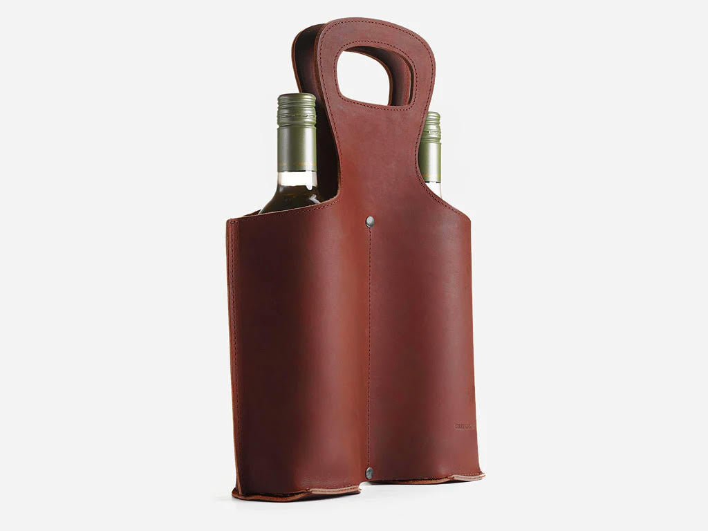 A brown leather wine tote bag holding two wine bottles, with sturdy handles and minimal metal rivets, set against a plain white background.