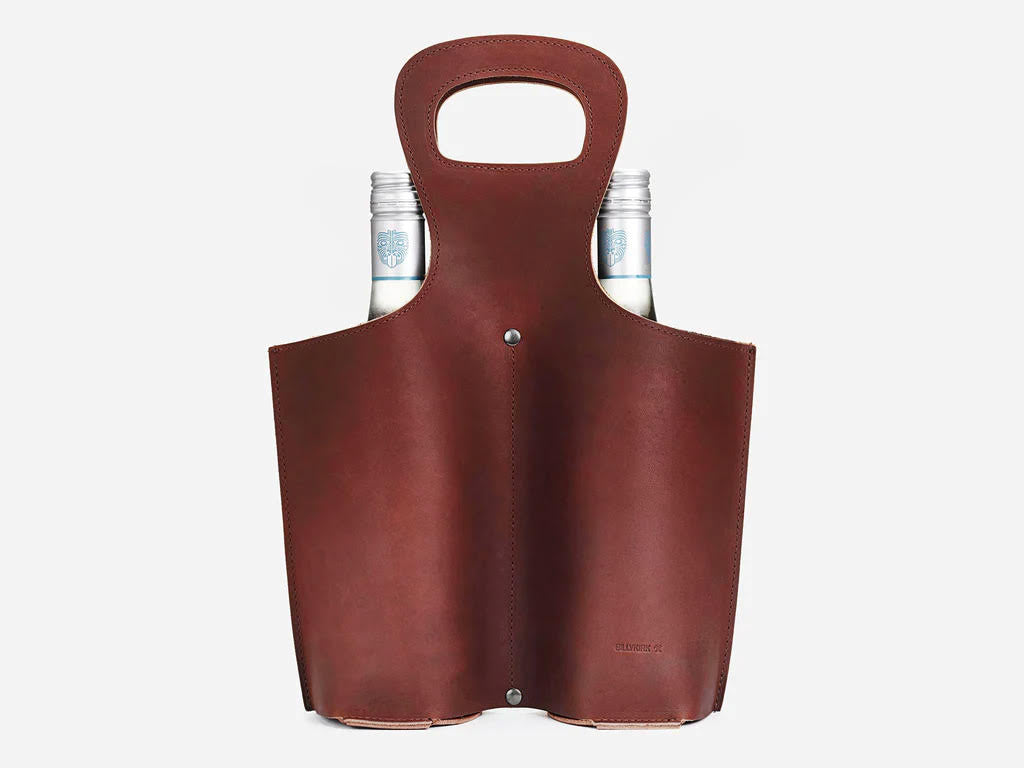 A brown leather wine carrier with a handle holds two glass bottles, with the necks and caps of the bottles visible above the top of the carrier. The background is white.